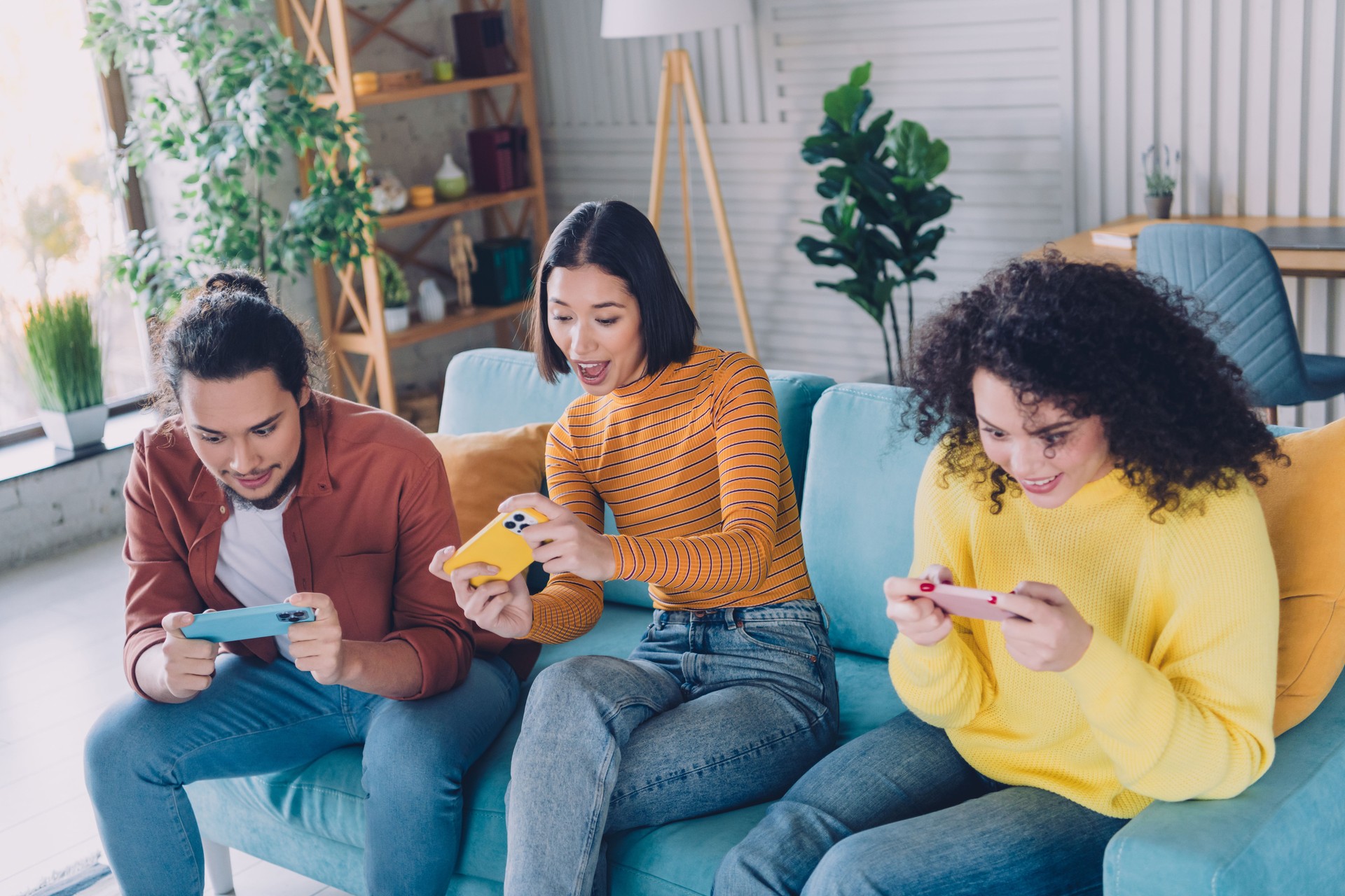 Group of diverse friends enjoying time together in a cozy living room, playing games on mobile devices on a casual day indoors